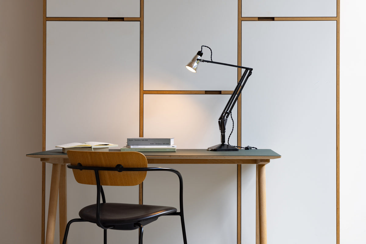 Anglepoise Navigation Edition Lamp sits on a desk table and illuminates the wall behind it
